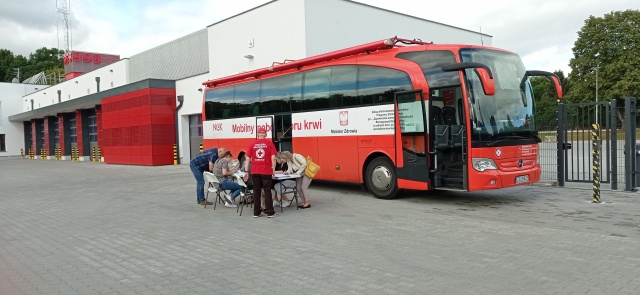 Na zdjęciu mobilny punkt poboru krwi (krwiobus), przed krwiobusem uczestnicy akcji wypełniają ankietę przy pomocy wolontariusza